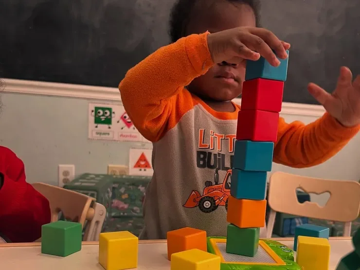 A child at Monumental Kids Academy building a tall tower with colorful blocks
