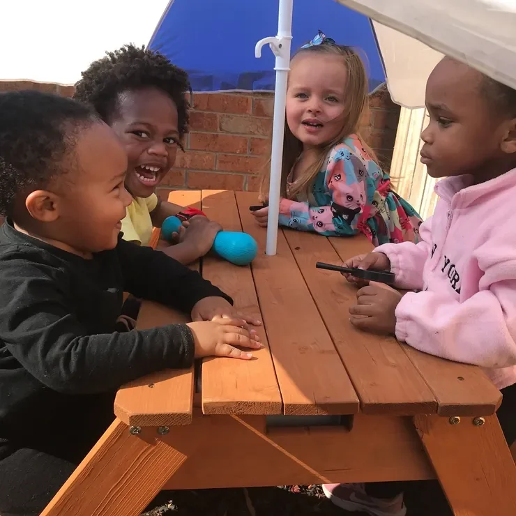 Children laughing together at an outdoor picnic table at Monumental Kids Academy